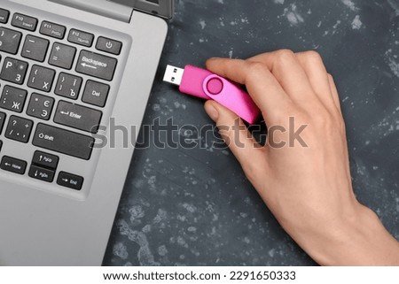 Woman using pink USB flash drive with modern laptop on black grunge background Royalty-Free Stock Photo #2291650333