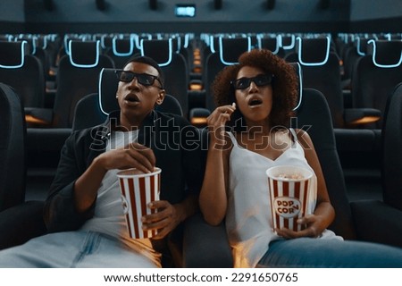 A loving couple looks surprised at the movie screen, enjoying popcorn during the cinema session. High quality photo