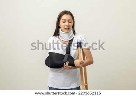 Depressed woman suffering from pain. Broken arm and leg. woman put on plaster cast splint with walking sticks crutches. Patient wearing sling support arm with neck collar. life insurance and accident Royalty-Free Stock Photo #2291652115