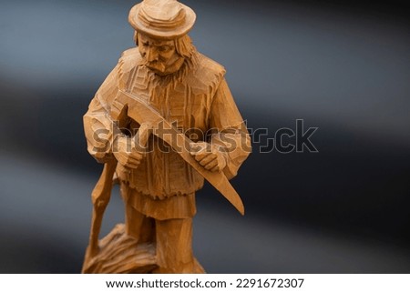 handmade wooden figurine on a black background. grandfather with a scythe in the hayfield