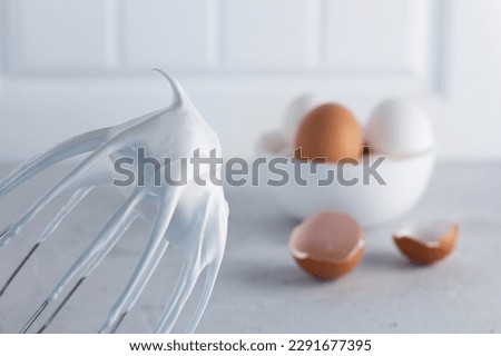 Whisked egg whites - whipped Italian meringue on a wire whisk and eggs on a gray background. copy space. Royalty-Free Stock Photo #2291677395