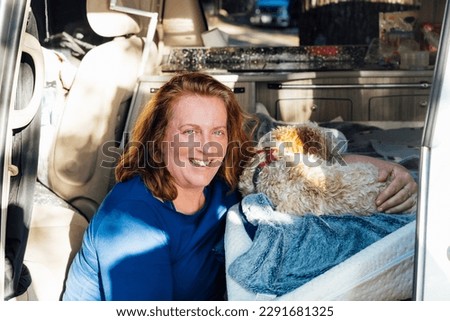 Portrait of middle-aged woman hugging her cockapoo puppy pet while sitting in van camper car vehicle during road trip. Best friend. Enjoying free lifestyle, vacation, freedom. Travel with pets