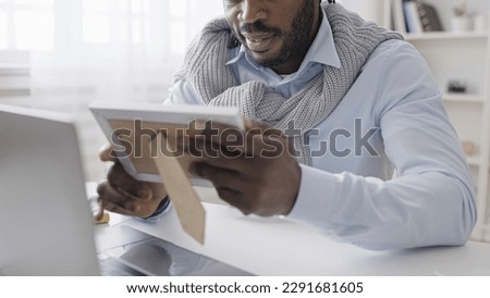 African American man working on laptop, taking a break to look at family photo on desk