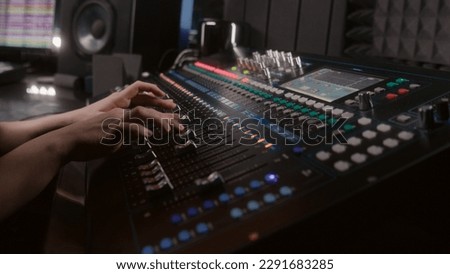 Audio engineer uses mixing console, remote control for adjusting sound, audio mixer. Musician changes the volume level, creates song with modern equipment. Sound recording studio. Music production.