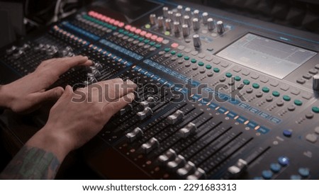 Close up hands shot of sound engineer using mixing console, remote control for adjusting sound, audio mixer. Musician changes the volume level, creates music. Sound recording studio. Music production.