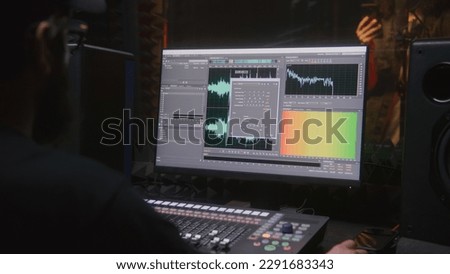 Sound engineer, producer uses control mixing surface. Computer screen shows DAW software interface for creating music. Singer records song in soundproof room. Sound recording studio. Music production.