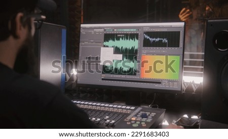 Sound engineer, producer uses control mixing surface. Computer screen shows DAW software interface for creating music. Singer records song in soundproof room. Sound recording studio. Music production. Royalty-Free Stock Photo #2291683403
