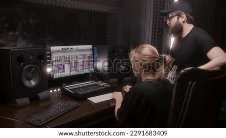 Sound engineer and producer, man and woman, create song in recording room. Computer screen showing DAW program interface with sound tracks. Modern sound recording studio equipment. Music production.