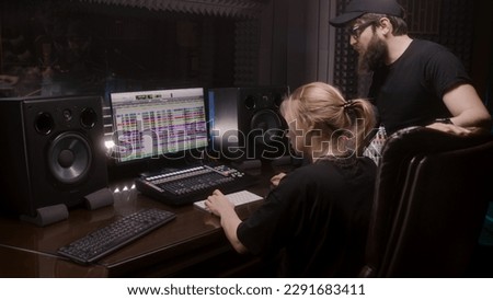 Sound engineer and producer, man and woman, create song in recording room. Computer screen showing DAW program interface with sound tracks. Modern sound recording studio equipment. Music production.