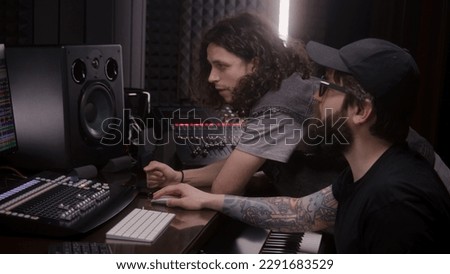 Audio engineer and male singer create song in music recording room. Computer screen showing program interface and tools for creating music. Modern sound recording studio equipment. Music production.