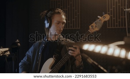 Musical band records song in sound recording studio. Male guitarist in headphones plays the electric guitar. Close up of drummer playing the drums. Music recording room. Music production concept.