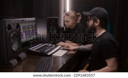 Audio engineer and producer, man and woman, create song in recording room. Computer screen showing DAW software interface with sound tracks. Modern sound recording studio equipment. Music production.