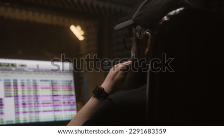 Sound engineer sits at computer and edits song in professional recording studio. Program and tools for creating music on PC monitor. Work in music recording room. Music production concept. Back view.