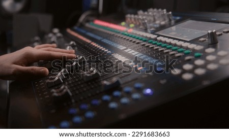 Audio engineer uses mixing console, remote control for adjusting sound, audio mixer. Musician changes the volume level, creates song with modern equipment. Sound recording studio. Music production.