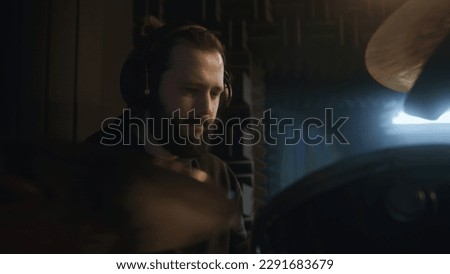 Male musician in headphones plays a drum kit. Drummer records song for musical rock band album in sound recording studio. Work in the music recording room. Music production concept. Zoom in.