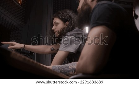 Audio engineer and male singer talk and create song in music recording room. Producer and musician listen finished recorded new album track. Work in sound recording studio. Music production concept.