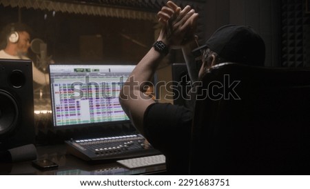 Sound engineer applauds to professional singer and works with digital audio workstation software by computer. African american man creates new song in audio recording studio. Music production concept.
