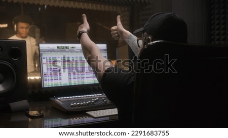 Sound engineer applauds to professional singer and works with digital audio workstation software by computer. African american man creates new song in audio recording studio. Music production concept.