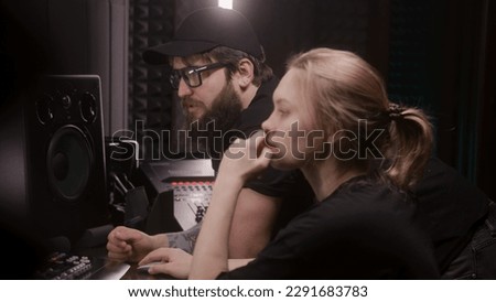 Female audio engineer uses mixing board, creates new song or DJ set with producer in sound recording studio. Computer screen showing DAW software interface with sound tracks. Music production concept.
