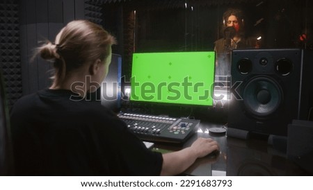 Male singer records song in soundproof room. Female audio engineer, producer uses control mixing surface. Computer screen showing DAW software with sound tracks. Sound recording studio. Green screen.