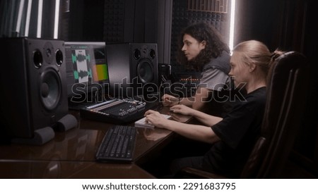 Female audio engineer and singer create song in music recording room. Computer screen showing program interface and tools for creating music. Modern sound recording studio equipment. Music production.