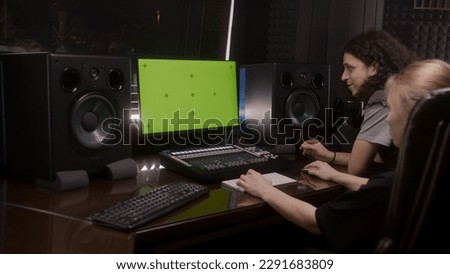 Computer screen showing DAW software interface. Female audio engineer and singer create song in music recording room. Modern sound recording studio equipment. Music production. Green screen on PC