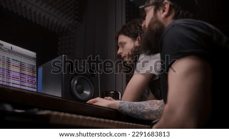 Audio engineer and male singer talk and create song in music recording room. Producer and musician listen finished recorded new album track. Work in sound recording studio. Music production concept.