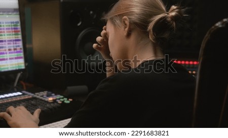 Experienced audio engineer or producer works in sound recording studio. Woman uses mixing console and digital audio workstation software to create new song. Program for recording music on PC monitor.