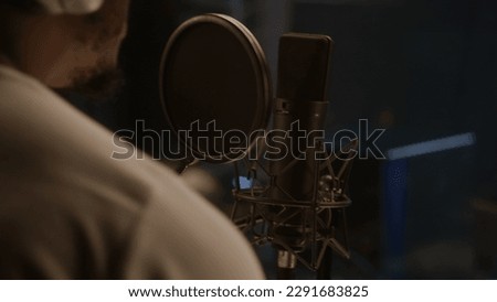 Close up shot of African American singer dancing and singing lyrical composition into microphone in soundproof room. Professional vocalist works in sound recording studio. Concept of music production. Royalty-Free Stock Photo #2291683825