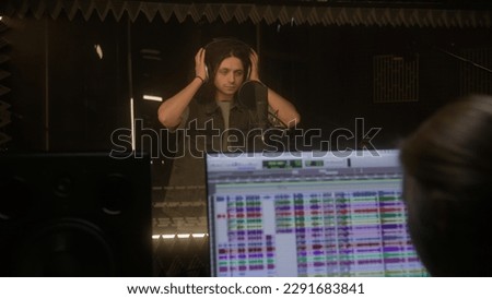 Vocalist in professional headphones sings lyrical composition into microphone in sound recording studio. Program and tools for creating music on computer monitor. Digital audio workstation software.