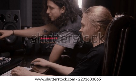 Female audio engineer and musician create song in music recording room. Computer screen showing DAW software interface with sound track. Modern equipment in sound recording studio. Music production.
