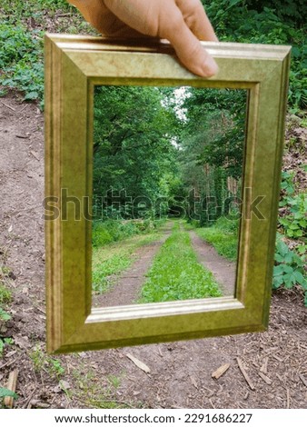 A mirror is held by a male hand on a forest path, the further forest path can be seen in the mirror.