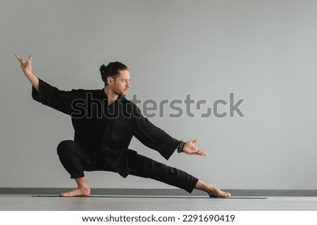 A man in black kimano practicing qigong energy exercises indoors.