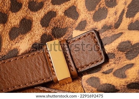 Detail of leather handbag, bright color of exotic skin of leopard, strap with golden metallic buckle. Texture and fashionable modern background