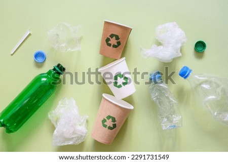 The concept of replacing plastic with environmentally friendly biodegradable materials. Paper cups with a recycling sign next to plastic trash.