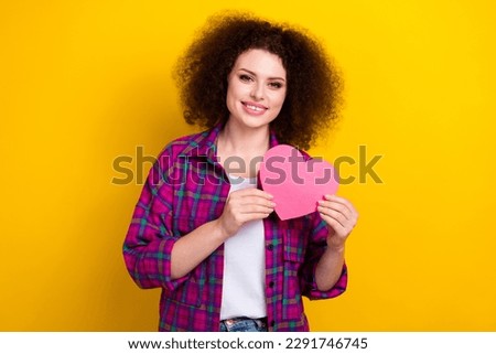 Photo of cheerful pretty woman dressed plaid shirt holding pink heart isolated yellow color background