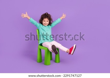 Full length photo of excited funky small kid wear turquoise shirt sitting chair rising hands arms empty space isolated violet color background Royalty-Free Stock Photo #2291747127