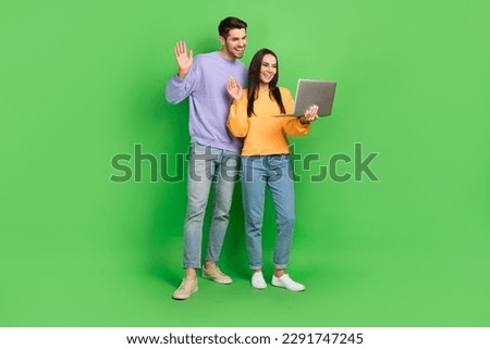 Full body photo of two positive people hold use netbook video call arm palm waving hi isolated on green color background