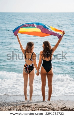 Female friends with rainbow flag on beach