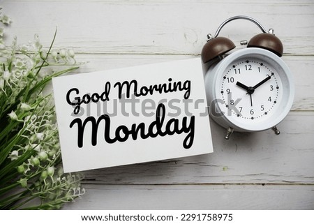 Good Morning Monday text message with flower and alarm clock on wooden background