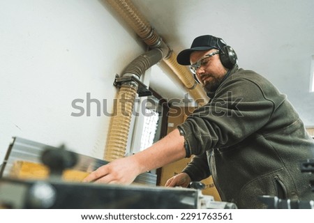 Carpenter during work. Focused male woodworking craftsman in protective gear using table saw. Low angle view. High quality photo