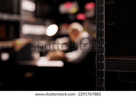 Evidence room equipped with metallic shelves full with federal documents. In background old police officer working overtime at criminal case, analyzing investigation report. Selectiv focus concept Royalty-Free Stock Photo #2291767883