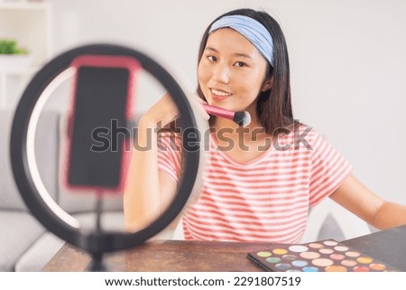 Asian woman doing her makeup looking flirtatiously at the camera