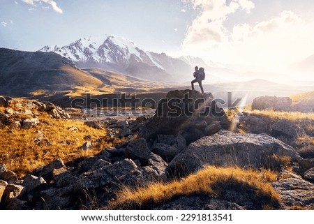 Small Man tourist with big backpack is walking climb in the mountain valley with snowy peaks at sunset cloudy sky background in Central Asia, Kazakhstan Royalty-Free Stock Photo #2291813541