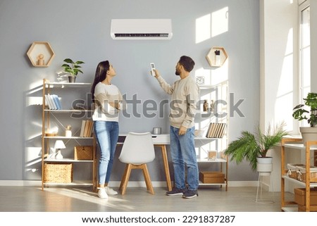 Family couple using a convenient air conditioning system at home. Young husband and wife setting up a comfortable temperature on their modern AC air conditioner on the wall in the living room Royalty-Free Stock Photo #2291837287