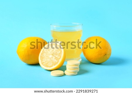 Glass of vitamin C effervescent tablet dissolved in water and lemons on blue background