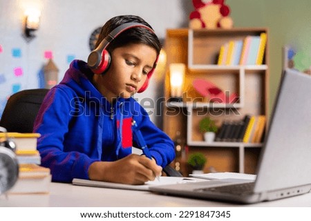 Indian kid making notes from online class on green screen laptop at home - concept of e-learning, intelligence and education