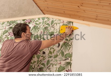 A worker pastes wallpaper on the walls in a room. Royalty-Free Stock Photo #2291851081