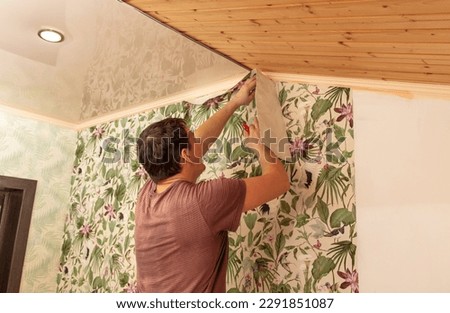 A worker pastes wallpaper on the walls in a room. Royalty-Free Stock Photo #2291851087