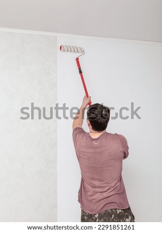A worker pastes wallpaper on the walls in a room. Royalty-Free Stock Photo #2291851261